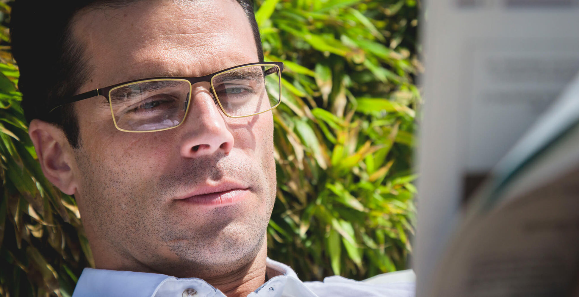 Man wearing Free Form Eyewear™ Titanium 14g feather-light eyeglasses model FFA945 in green full frame while reading outdoors. Luxury German design for men.